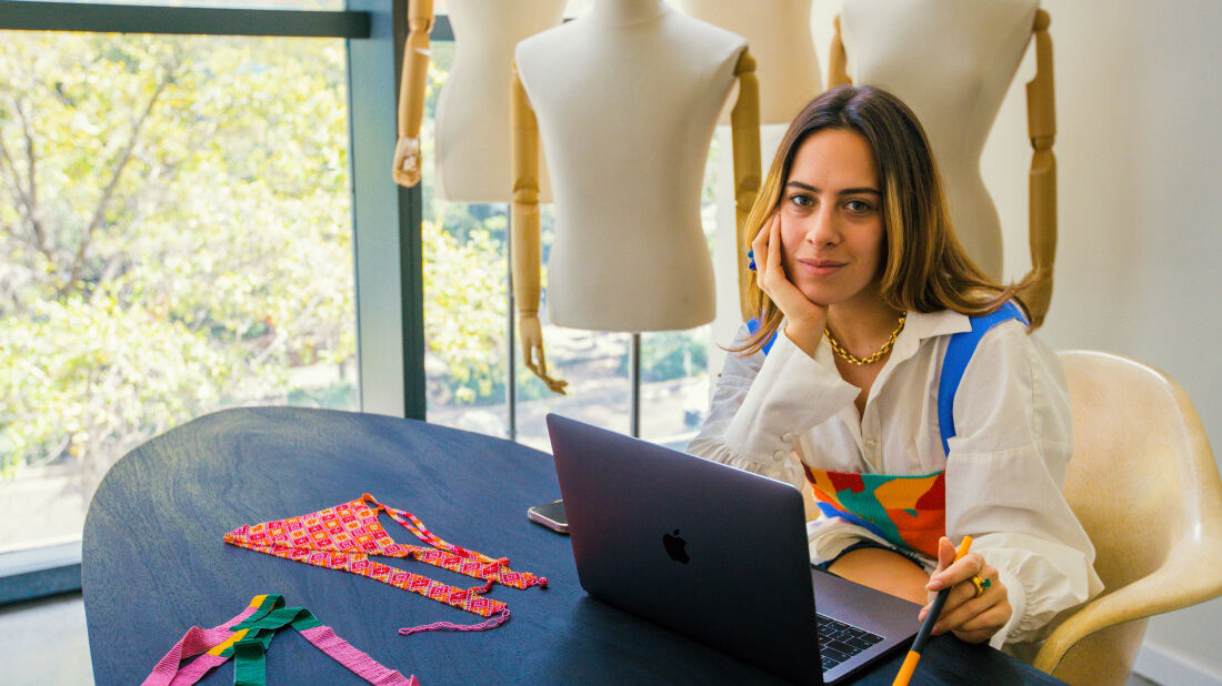 Designer with laptop, textiles, and mannequins in a bright studio."