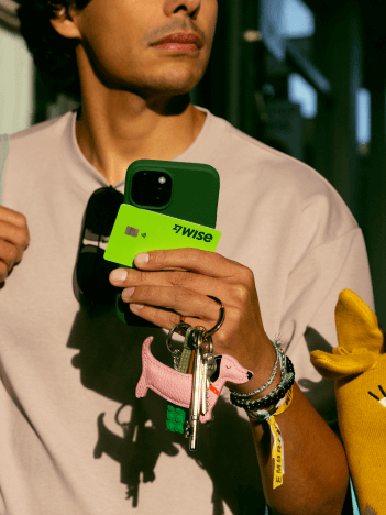 Ein Mann geht eine Einkaufsstraße entlang. Er hält sein Telefon, seine Schlüssel, seine Sonnenbrille und eine Wise-Karte in der Hand.